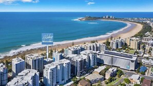 Une zone hôtelière située sur la côte, avec de grands immeubles, une plage et un panneau indiquant « Holiday Mooloolaba ».