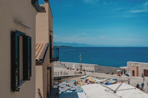 Vista costera con un muro de piedra, sombrillas de playa y un mar azul y transparente.