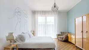 A bedroom with a bed, bedside table, lamp, chair, wardrobe, and a window with sheer curtains. - Sant'Isaia Apartment by Wonderful Italy (Bologna)