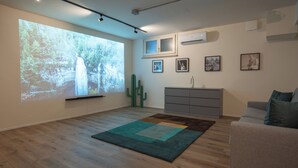 A modern living room with a large projection screen, a cactus, a grey sofa, and a wooden floor. - Suite Veronetta (Verona)