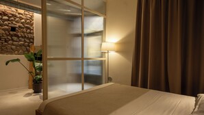A hotel room with a bed, a potted plant, a stone wall, and a window with curtains. - Suite Veronetta (Verona)