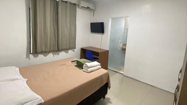 Habitación de hotel con cama, televisor de pantalla plana montado en la pared, aire acondicionado, escritorio con silla y puerta corredera de vidrio que da a un baño.