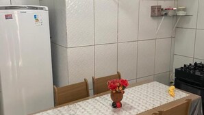 Una cocina compacta con refrigerador, una mesa de comedor con sillas, un estante de vidrio y un pequeño florero con flores.