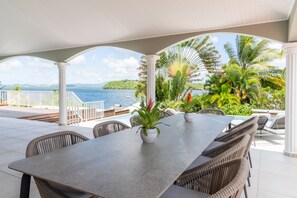 An outdoor patio with a table and chairs, surrounded by lush greenery and a view of the sea. - Bel Embrun - Villa Iléenne (Les Trois-Ilets)