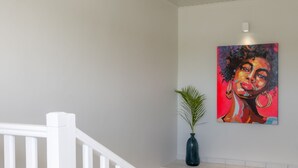 A staircase with white railings leading to a landing with a potted plant and a colorful painting. - Bel Embrun - Villa Iléenne (Les Trois-Ilets)