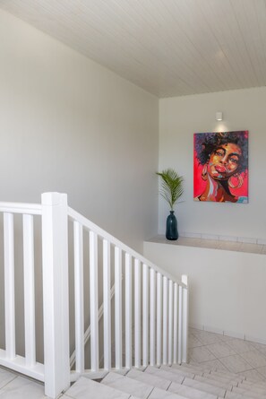 A staircase with white railings leading to a landing with a potted plant and a colorful painting. - Bel Embrun - Villa Iléenne (Les Trois-Ilets)