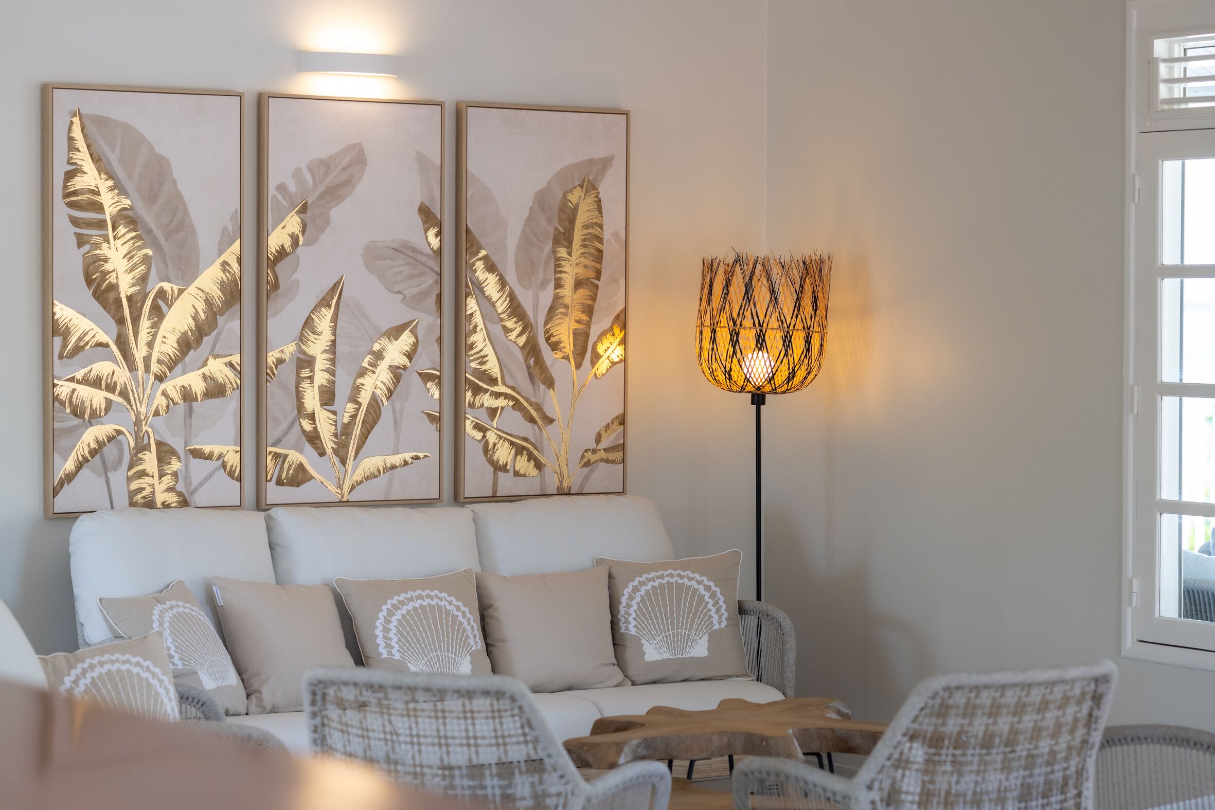 A modern living room with a sofa, two armchairs, a coffee table, and a floor lamp. There are three framed leaf artworks on the wall.