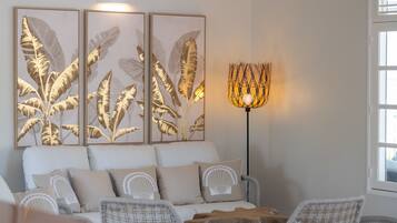 A modern living room with a sofa, two armchairs, a coffee table, and a floor lamp. There are three framed leaf artworks on the wall.