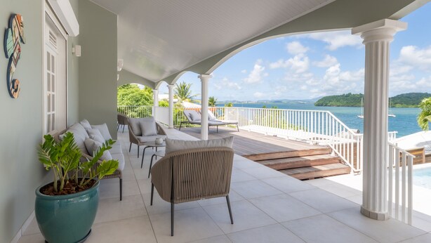 A covered outdoor area with a view of the sea, a large potted plant, and seating arrangements. - Bel Embrun - Villa Iléenne (Les Trois-Ilets)