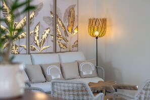 Una sala moderna con un sofá, cojines estampados, una lámpara de pie y una pared con diseños de hojas.