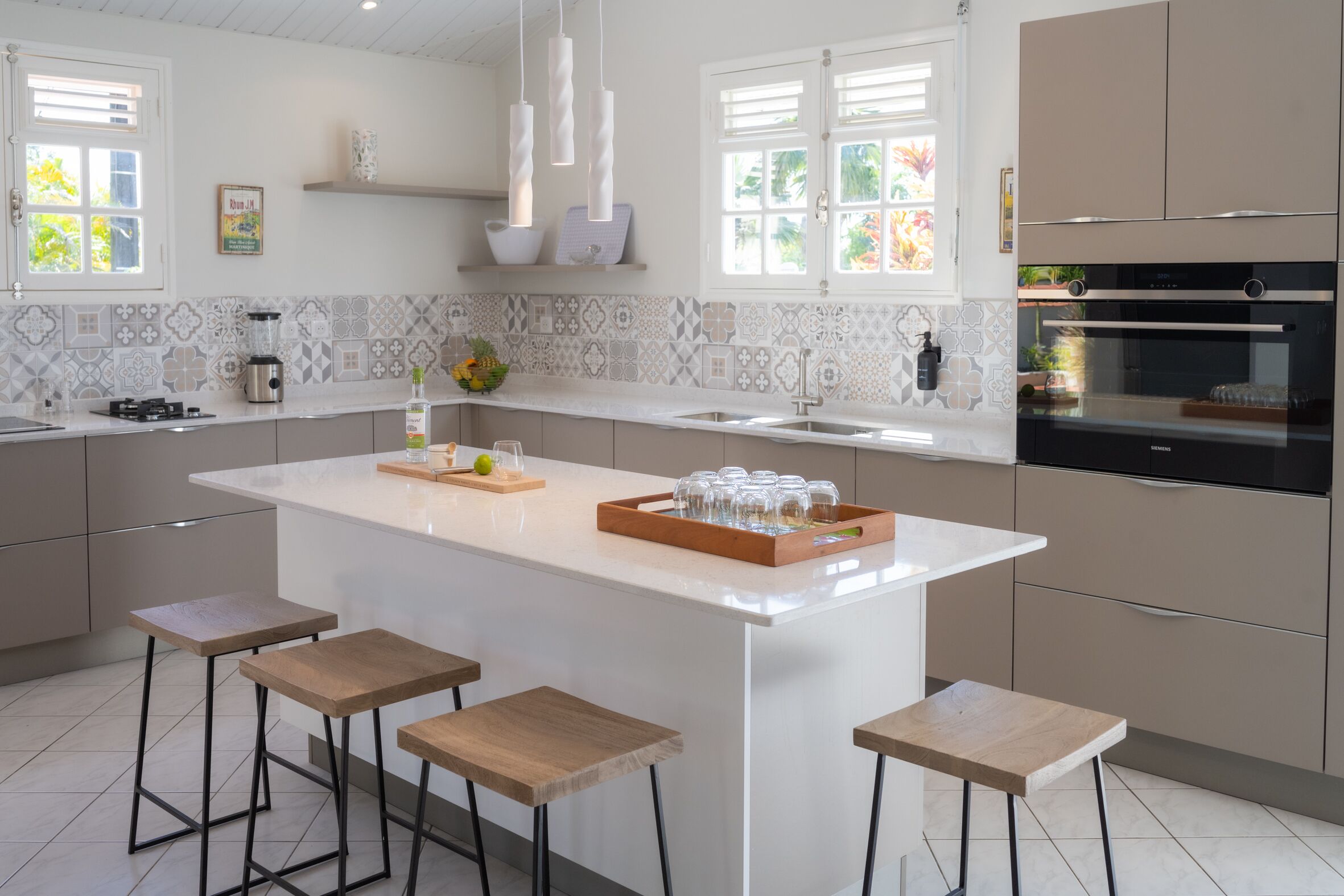 A modern kitchen with a large island, bar stools, a built-in oven, and a backsplash with geometric tiles.