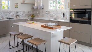 A modern kitchen with a large island, bar stools, a built-in oven, and a backsplash with geometric tiles. - Bel Embrun - Villa Iléenne (Les Trois-Ilets)