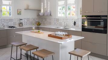 A modern kitchen with a large island, bar stools, a built-in oven, and a backsplash with geometric tiles.