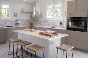 A modern kitchen with a large island, bar stools, a built-in oven, and a backsplash with geometric tiles.
