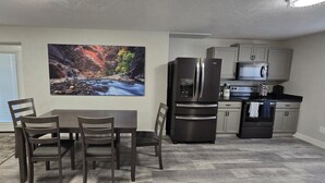 Cocina compacta con refrigerador, microondas y horno. Hay una mesa de comedor con sillas y un cuadro de una escena fluvial en la pared.