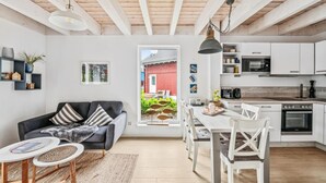 Moderni keittiö, jossa on valkoiset kaapit, mikroaaltouuni ja uuni. Olohuoneessa on ruokapöytä tuoleineen sekä sohva.