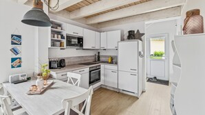 Moderni keittiö, jossa on valkoiset kaapit, puinen katto ja ruokailutila, jossa on valkoinen pöytä ja tuolit.