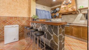 Una cocina con isla de piedra, taburetes de bar, un refrigerador y una pata de cocina colgante.