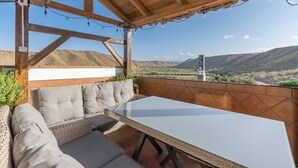 Un espacio al aire libre cubierto con una mesa, asientos acolchados y vistas a un valle.