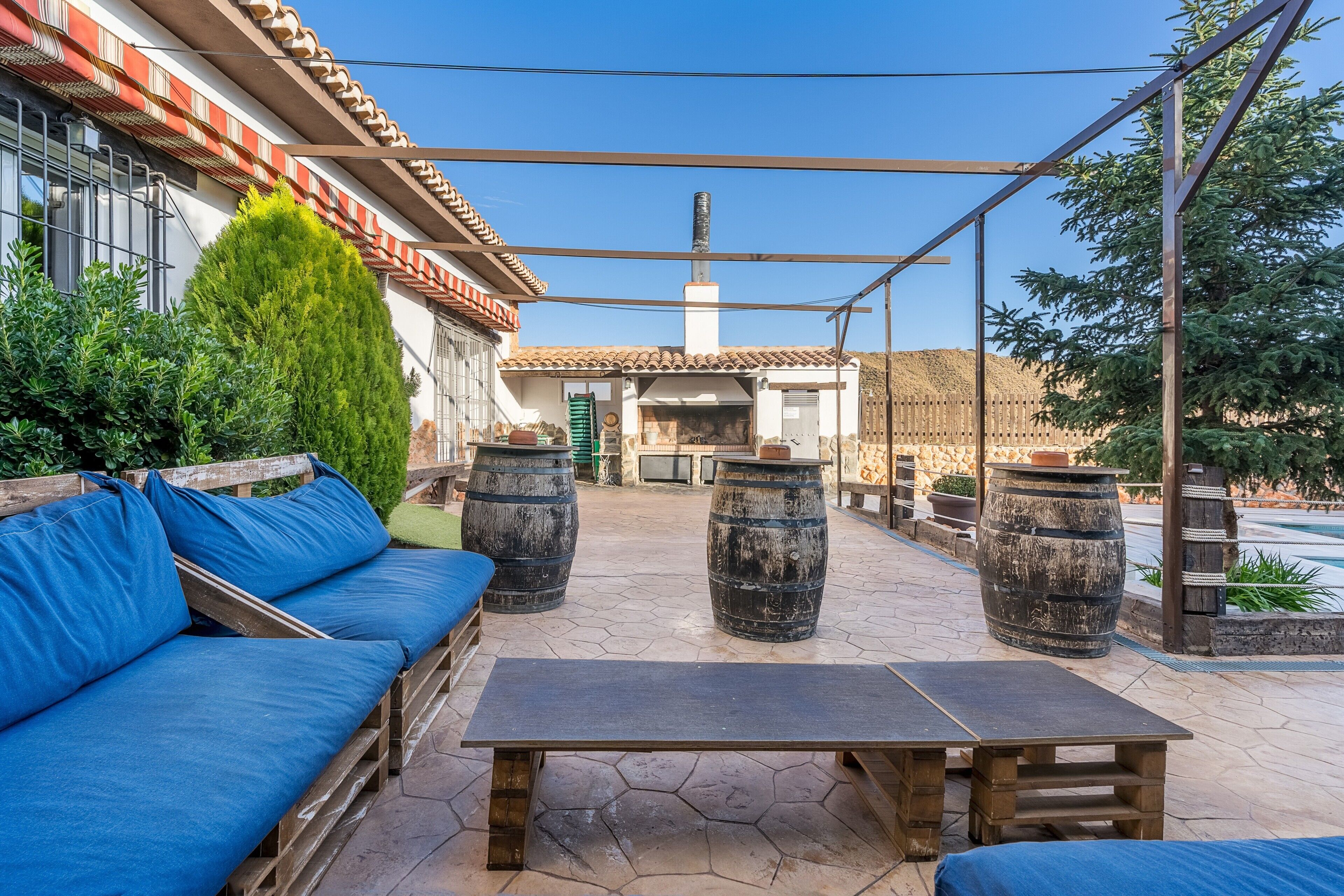Un patio al aire libre con un banco de madera, asientos azules acolchados y grandes barriles.