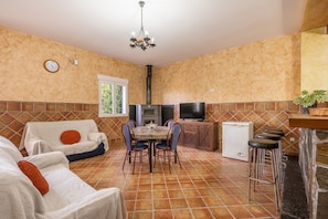 Una cocina con una mesa de comedor, sillas, un televisor, un refrigerador pequeño y una barra con taburetes.