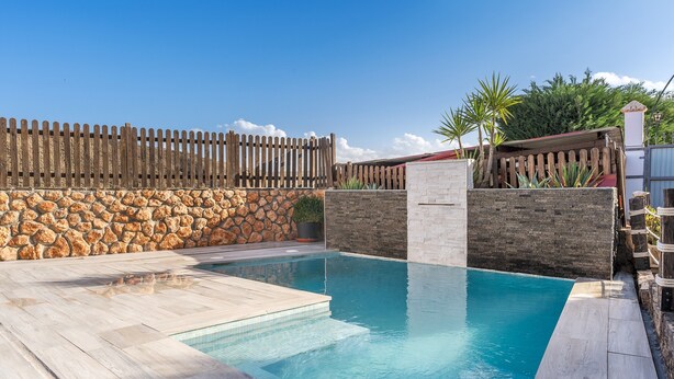 Una piscina con paredes de piedra, cerca de madera y un cielo azul despejado.