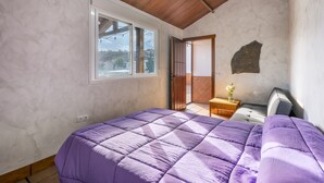 Un dormitorio con una cama grande, una ventana, techo de madera y una puerta que da a otra habitación.