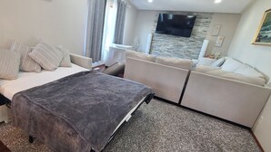 Ein modernes Wohnzimmer mit einer Couch, einem Bett mit grauer Decke und einem Flachbildfernseher, der an einer Steinwand befestigt ist.