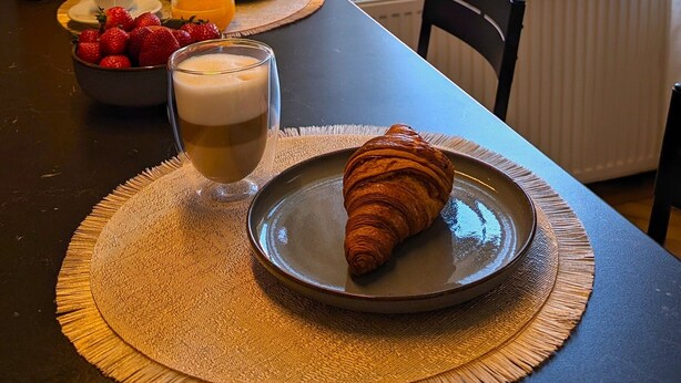 A breakfast setting with croissants, strawberries, and orange juice on a table by a window with a view of buildings. - Elegant Studio in the Historic Center, AC, Quiet Area (Sibiu)