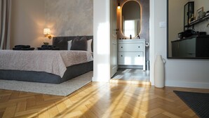A bedroom with a bed, bedside lamp, and a bathroom with a mirror, sink, and towel rack. - Elegant Studio in the Historic Center, AC, Quiet Area (Sibiu)