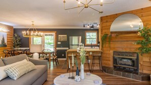 Una sala de estar acogedora con chimenea, paredes de madera, zona de comedor y una lámpara moderna.