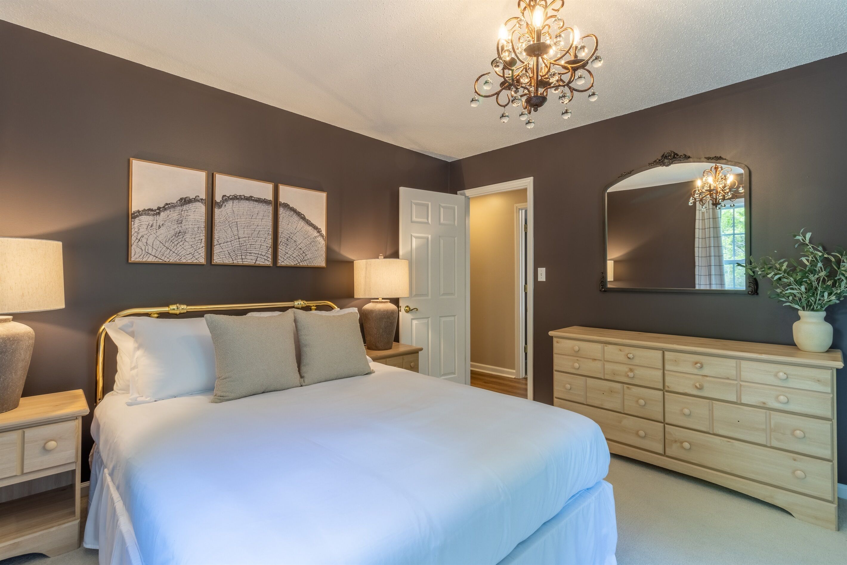 Une chambre à coucher comprenant un lit, des tables de chevet, une commode, un lustre et des œuvres d’art accrochées au mur.