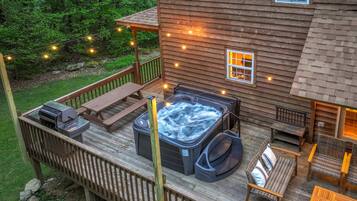 Una terraza de madera con un jacuzzi, asientos exteriores y luces colgantes.