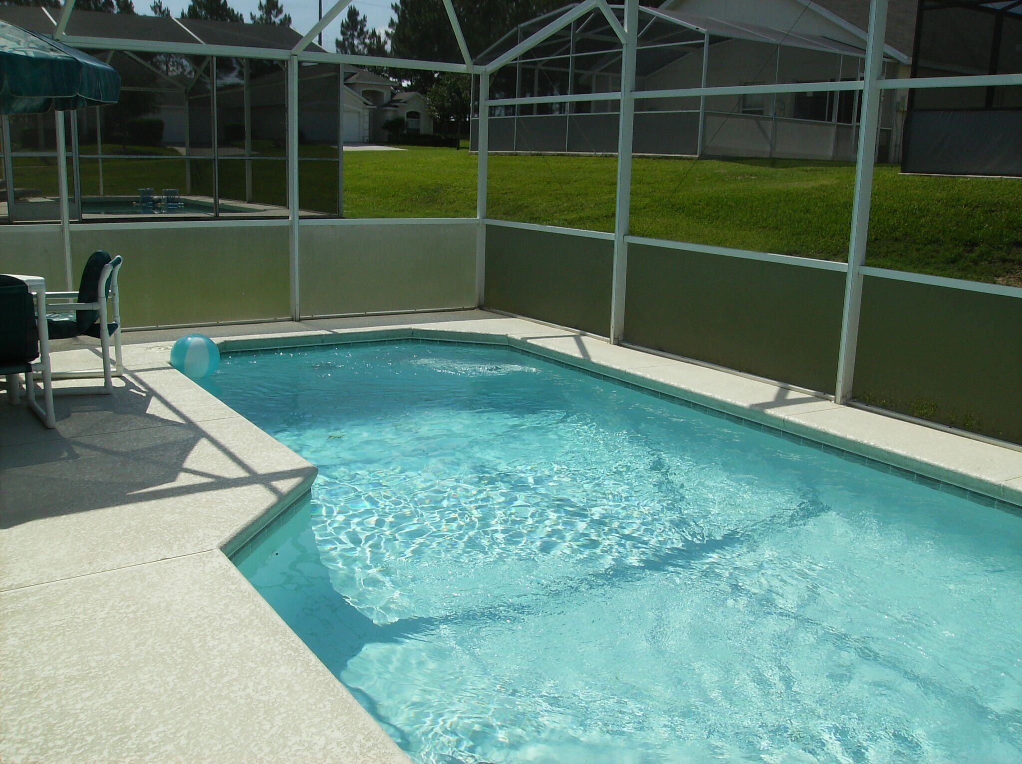 A rectangular swimming pool with clear blue water, surrounded by a white fence and a covered area with chairs.