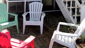 A wooden deck with a glass enclosure, white and red Adirondack chairs, and a white staircase leading to a door. - Beaufort Harbour Suites West Lodge (Beaufort)