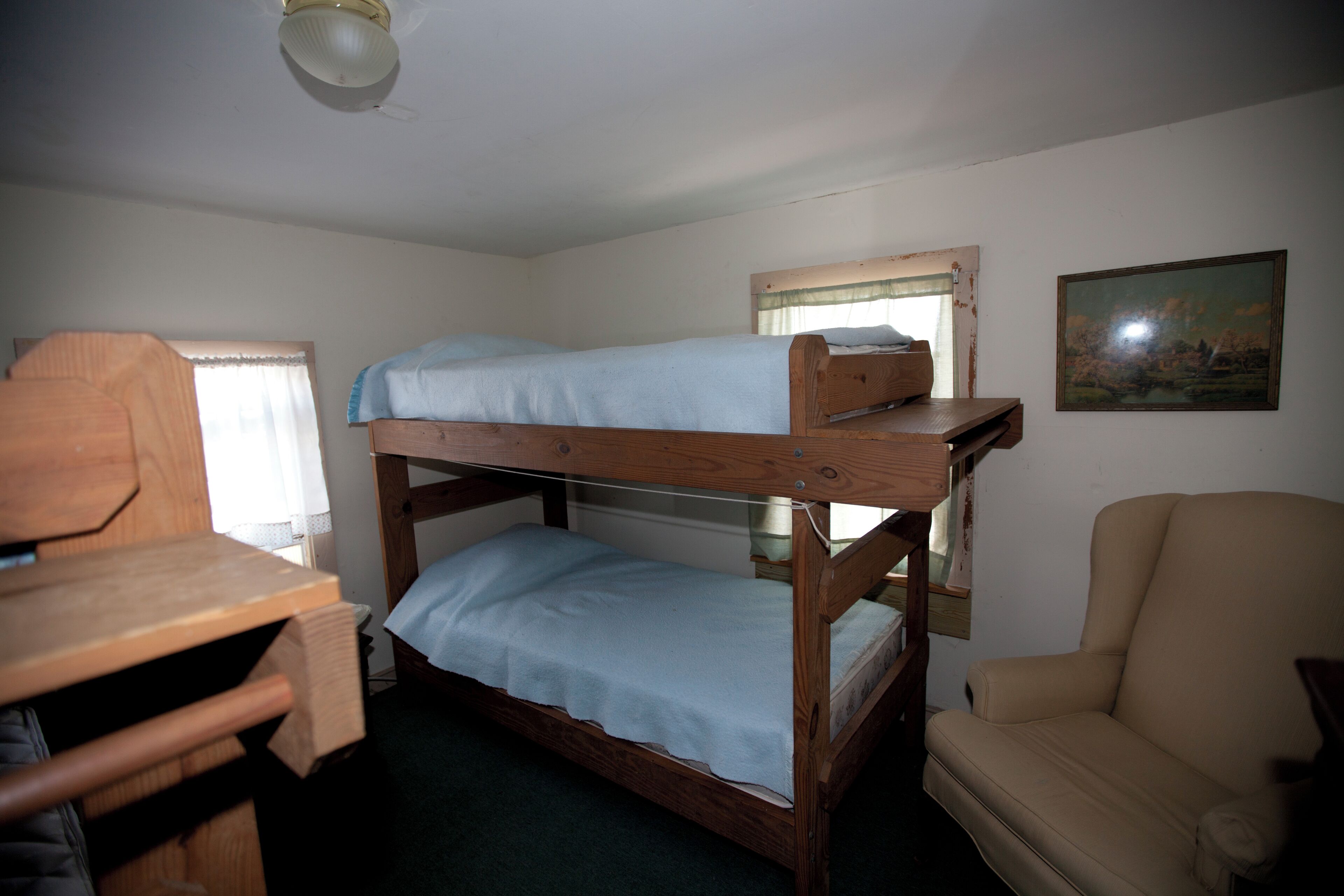 A bunk bed room with a desk and chair, a window with curtains, and a painting on the wall.