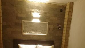 A bed with white bedding and a dark blue throw blanket, set against a stone wall with a framed picture above. - Terrific 4-bedroom hotel in Luxor with AC, WiFi and swimming pool  (Luxor)