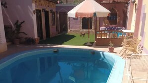 A swimming pool with a tiled edge, surrounded by a patio area with outdoor furniture and a covered seating area. - Terrific 4-bedroom hotel in Luxor with AC, WiFi and swimming pool  (Luxor)