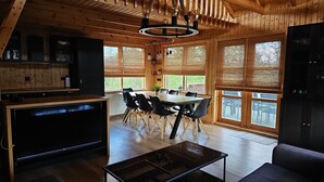 Eine moderne Küche mit Holzschränken, ein Essbereich mit Tisch und Stühlen sowie große Fenster mit Jalousien.