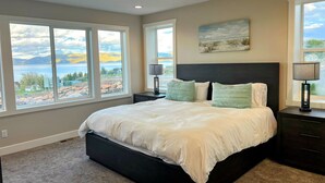 A bedroom with a large bed, two bedside tables, and a view of a lake.