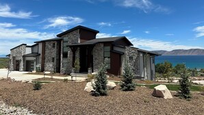 A modern two-story house with a stone facade, large windows, and a view of a lake.