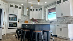 A modern kitchen with white cabinets, a marble backsplash, and a large island with bar stools.