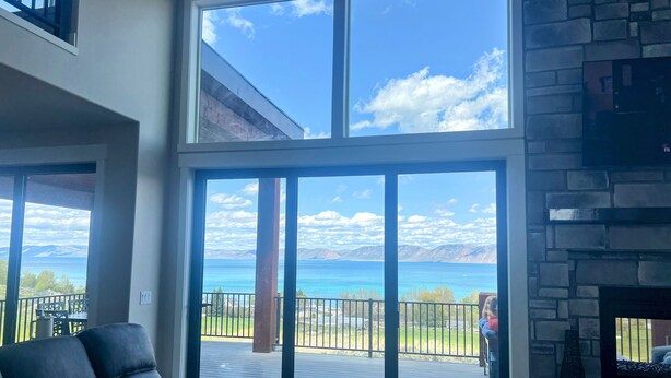 A spacious living room with a large sliding glass door leading to a deck with a view of a lake and mountains.