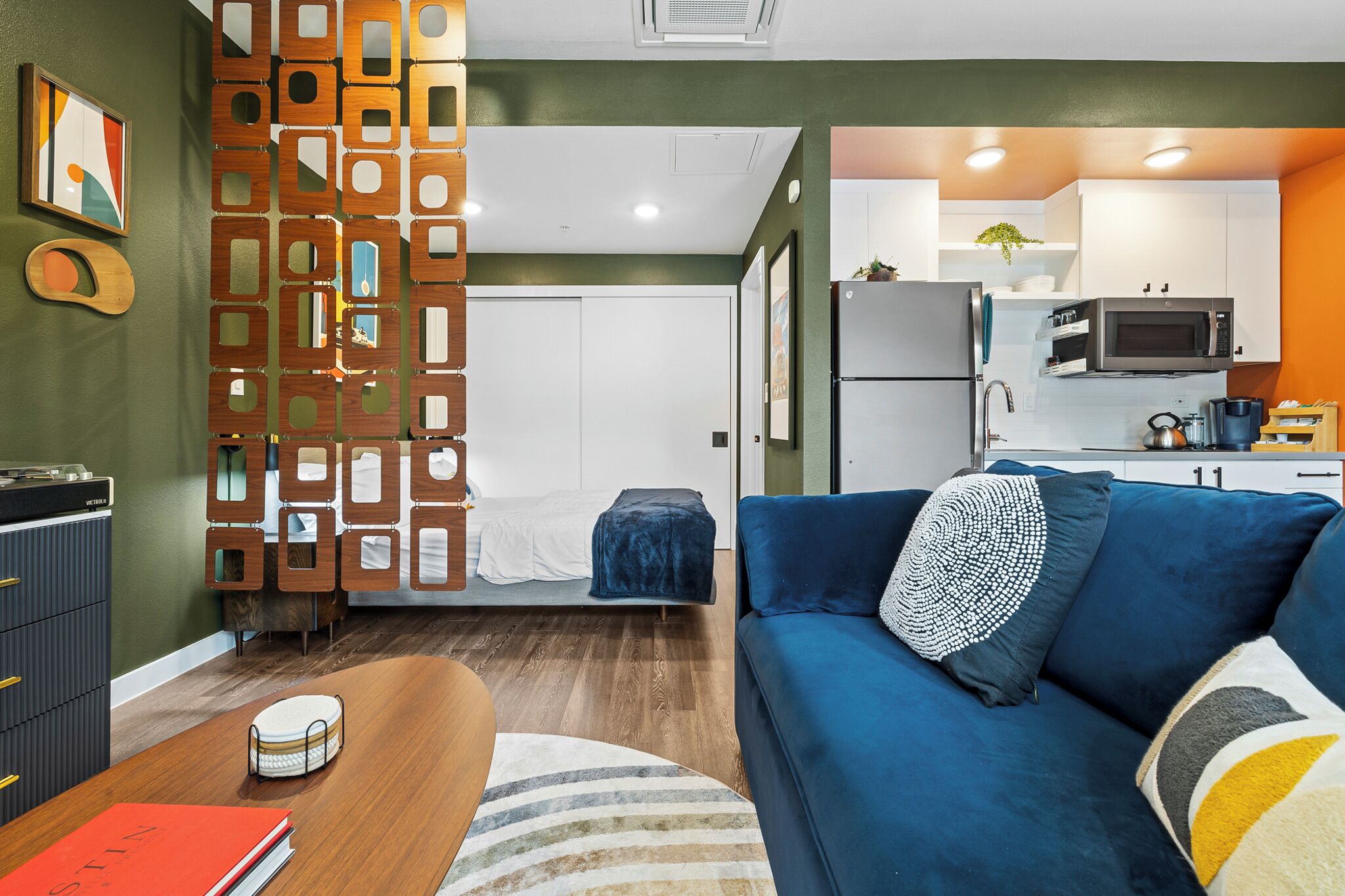 A compact living space with a kitchenette, a sofa, a bed, and a decorative partition.