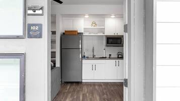 A compact kitchen with white cabinets, a stainless steel refrigerator, a microwave, and a wooden floor.