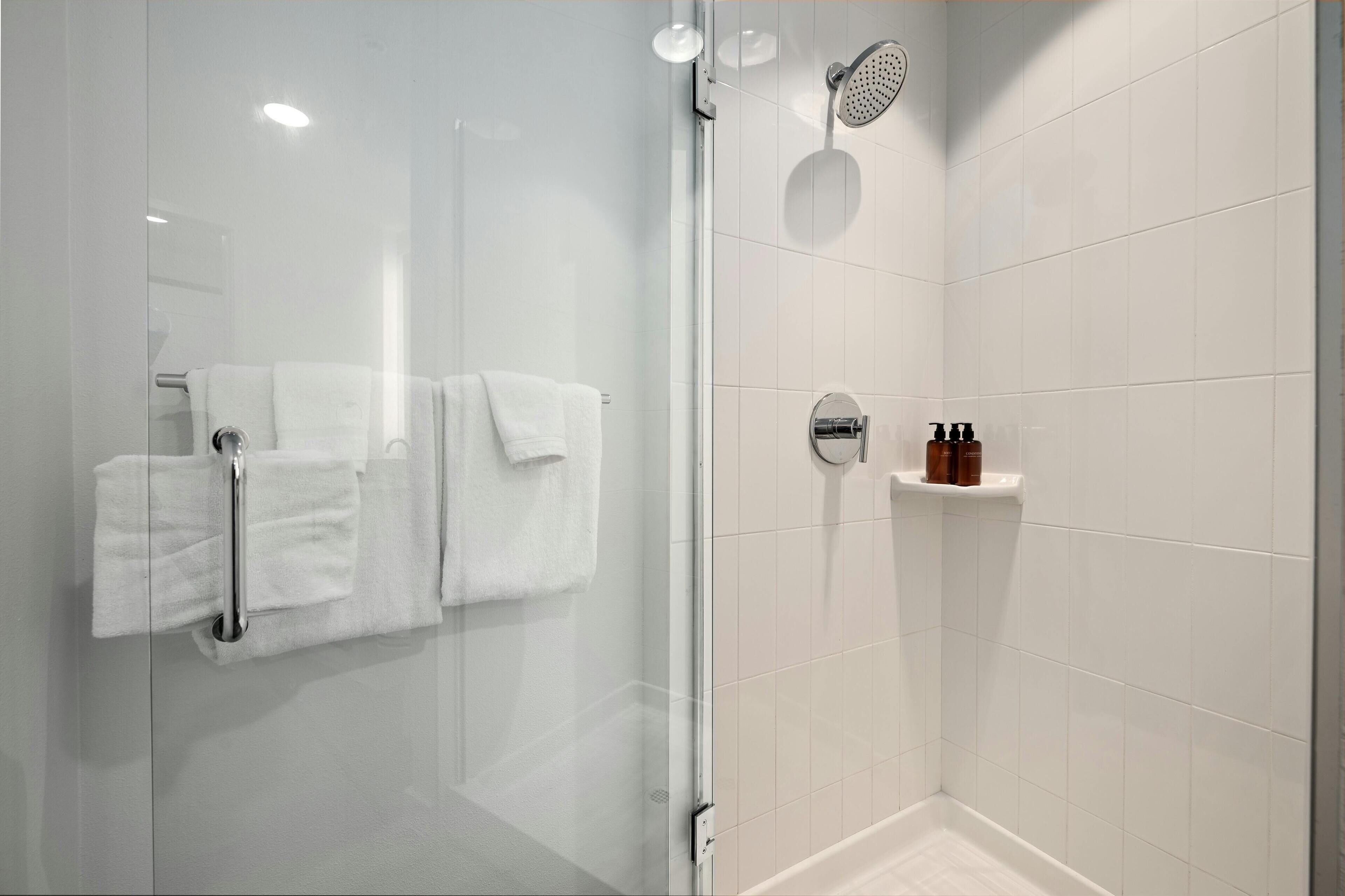 Un baño moderno con cabina de ducha de vidrio, azulejos blancos, un perchero con toallas dobladas y un dispensador de jabón en un estante.