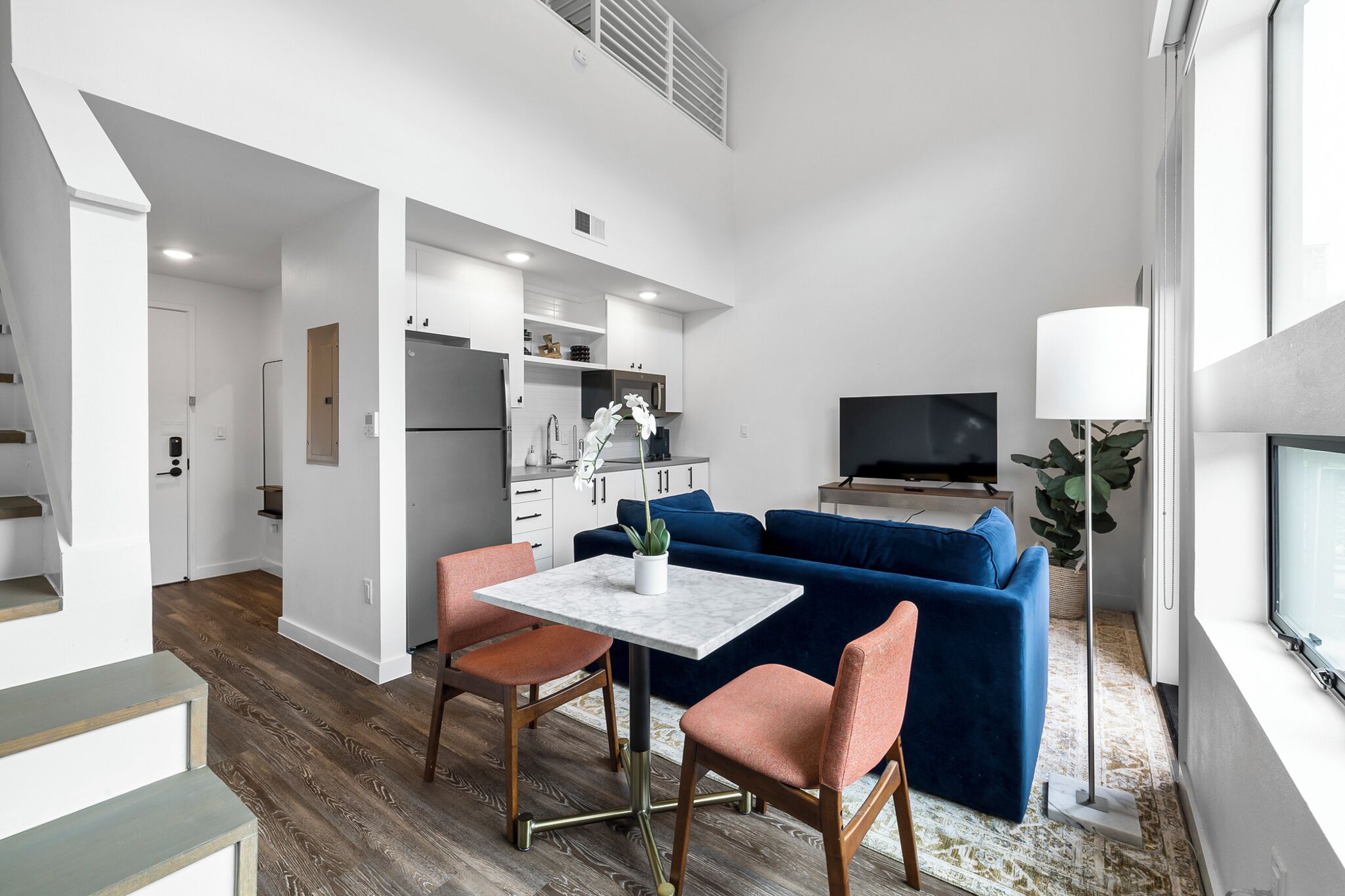 A modern apartment with a dining area, a living room with a blue sofa, and a kitchen.