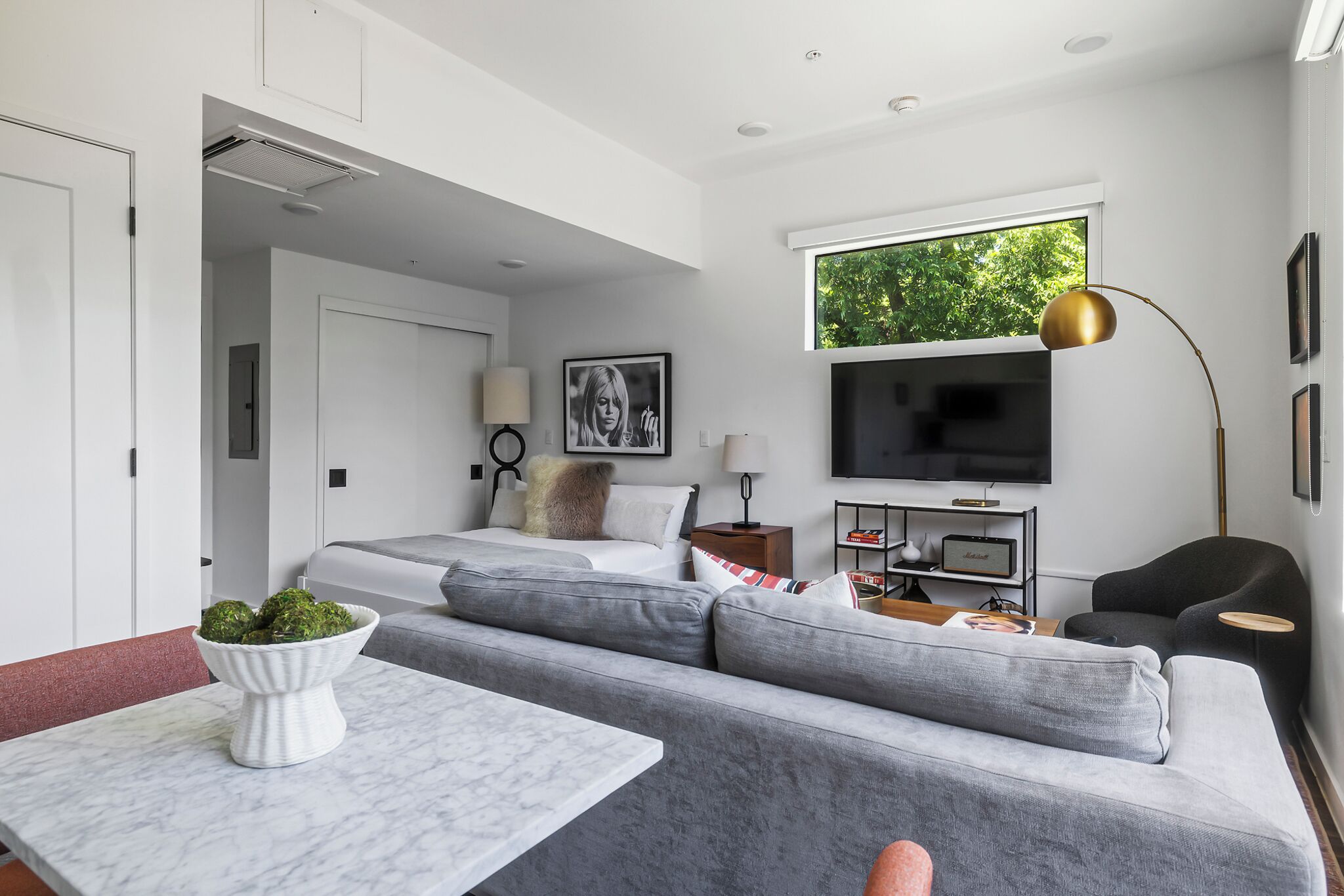 A modern bedroom with a bed, a TV, a sofa, and a dining area with a table.