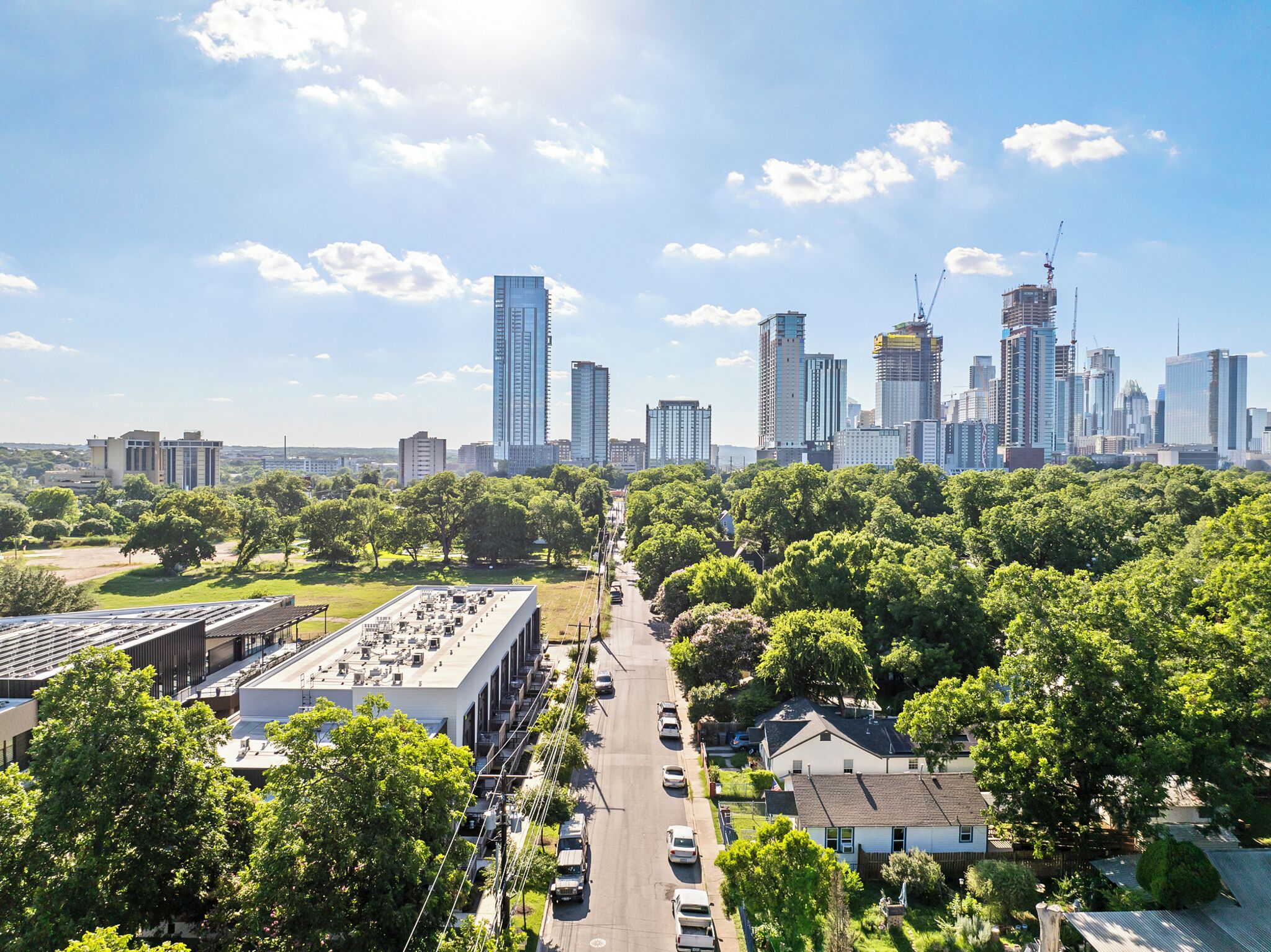 Stadsbeeld met moderne wolkenkrabbers, een combinatie van woon- en kantoorgebouwen, en een groen park met bomen.