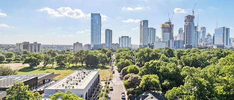 Stadsbeeld met moderne wolkenkrabbers, een combinatie van woon- en kantoorgebouwen, en een groen park met bomen.